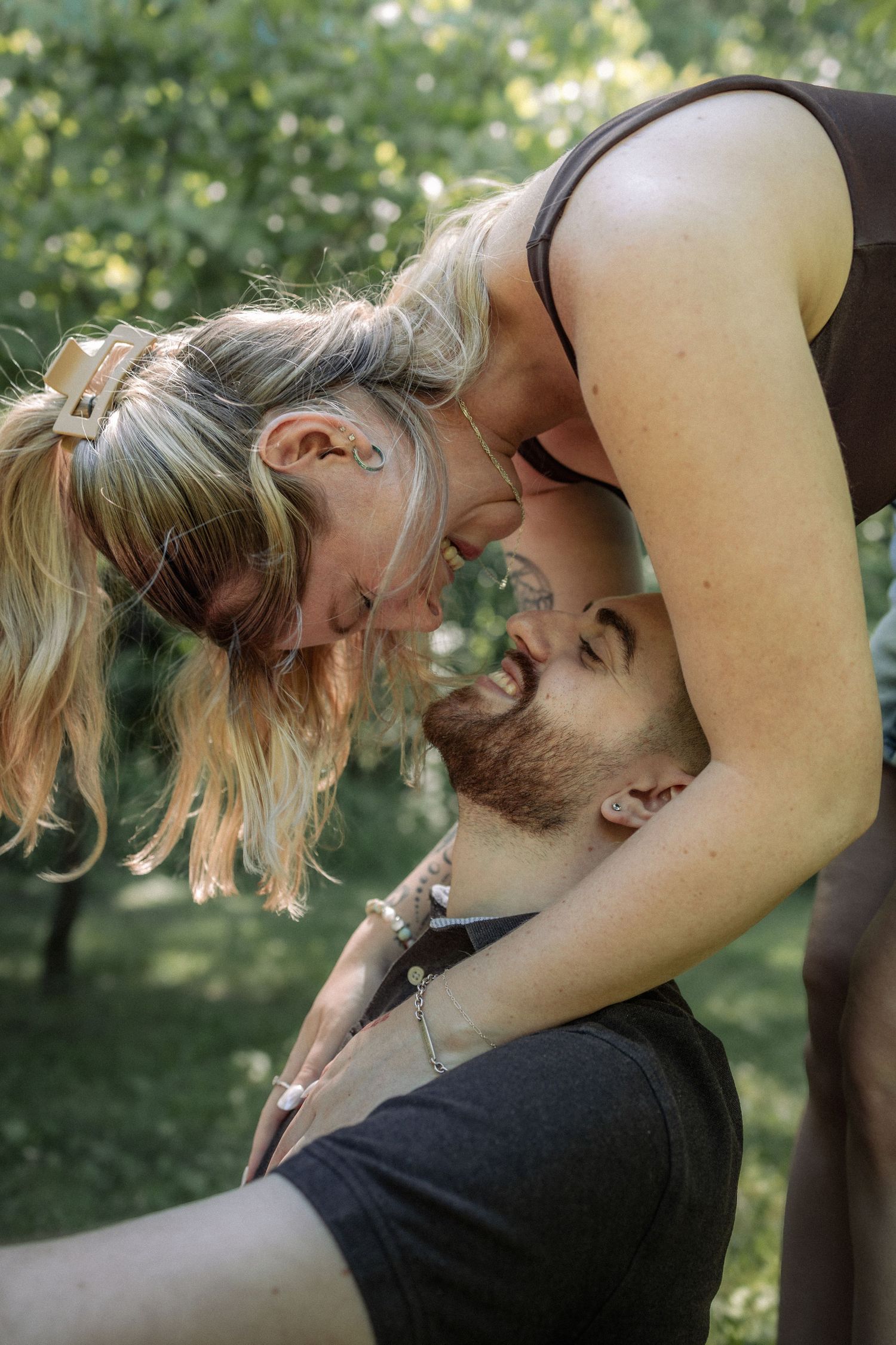 A happy couple shares a romantic moment outdoors, with a smiling bearded man and blonde woman leaning in close together.
