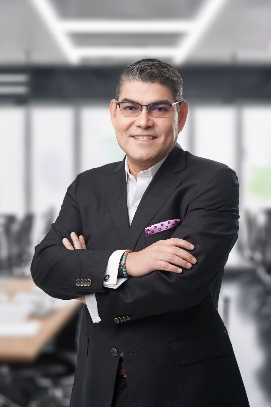 Headshot de consultor o financiero con lentes y pañuelo rosa sonriendo en entorno de oficina corporativa.