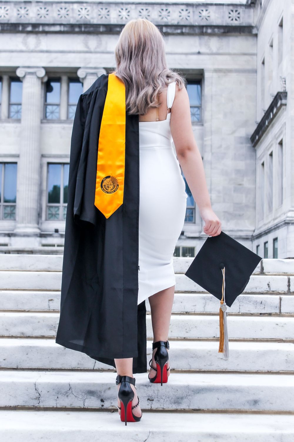 Graduate walking up stone steps in cap and gown with bright red heels.