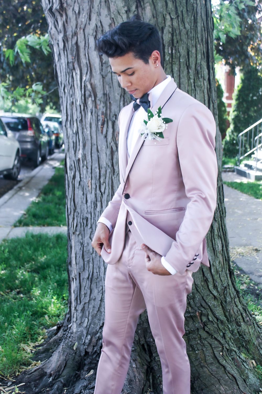 Person wearing a pink formal suit posing next to a large tree trunk.