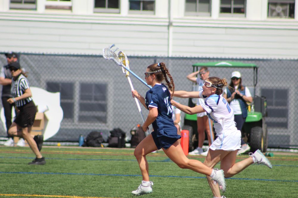 Women's lacrosse players compete for possession during an intense match on artificial turf field.