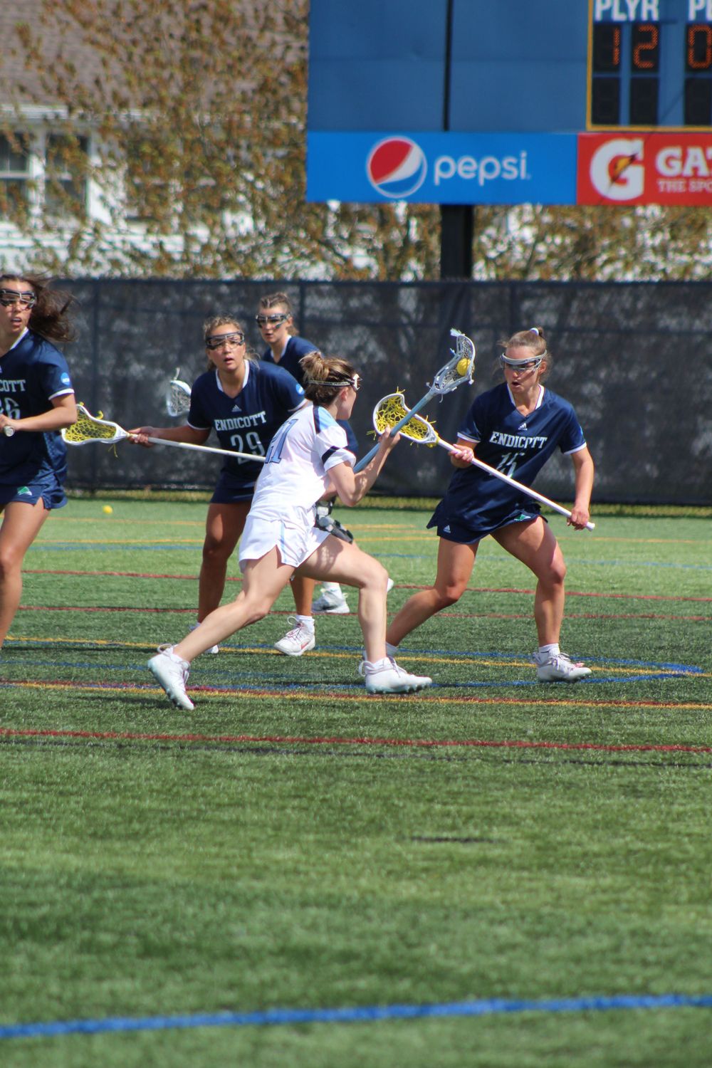 A lacrosse player maneuvers past defenders during a competitive match on a sports field.