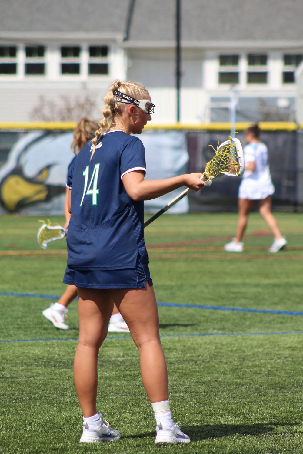 Lacrosse player in navy jersey number 14 holds stick while positioned on field.