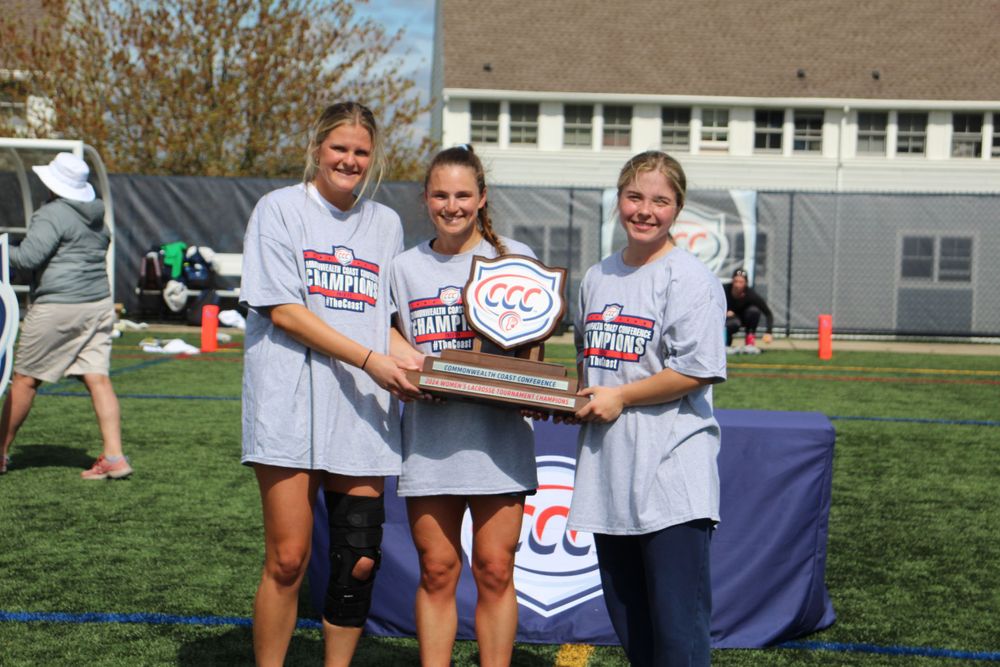 Three team members hold up their championship trophy on a sunny field.