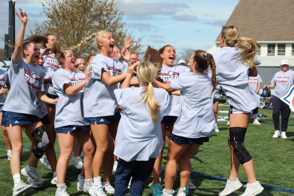 Athletic team celebrates victory together on sunny field with enthusiastic jumping and cheering.