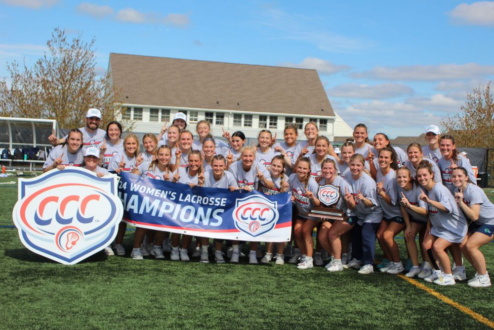 Team members gather on a field holding a championship banner during a victory celebration.