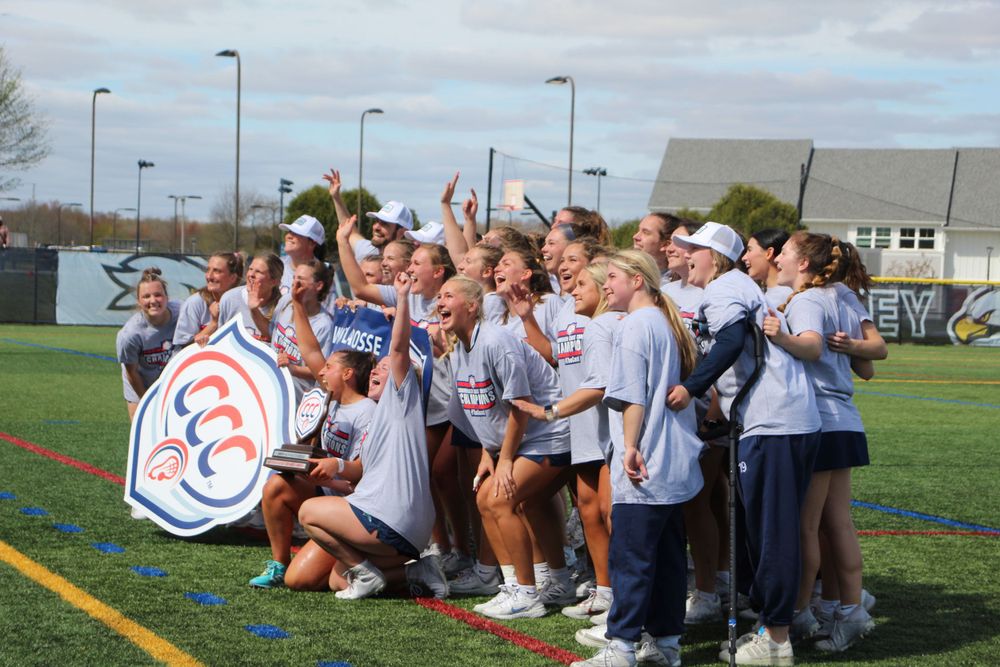 Sports team poses with championship banner and trophy during outdoor celebration.