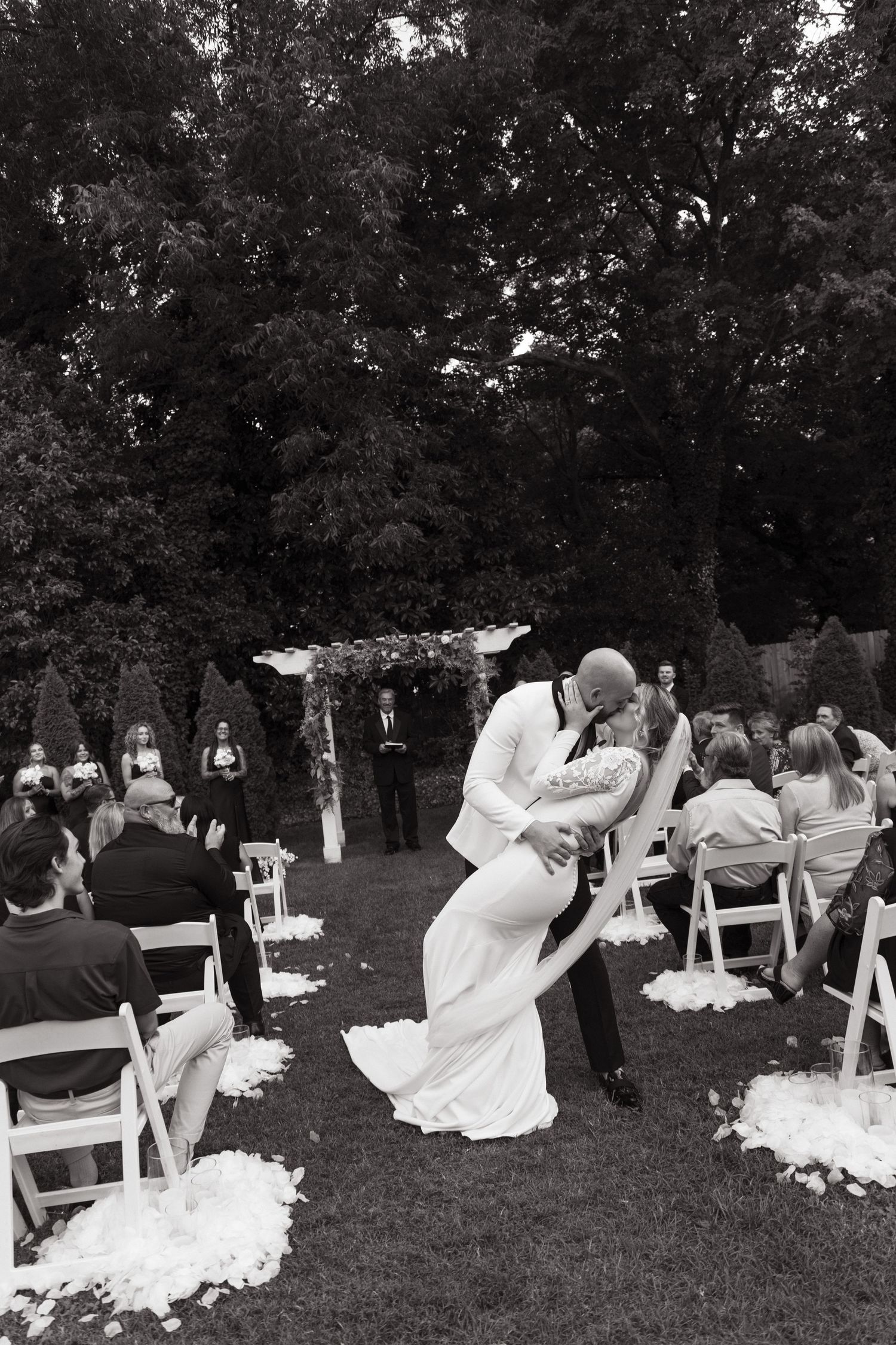 A romantic outdoor wedding ceremony with a couple sharing their first kiss as trees provide a scenic backdrop.