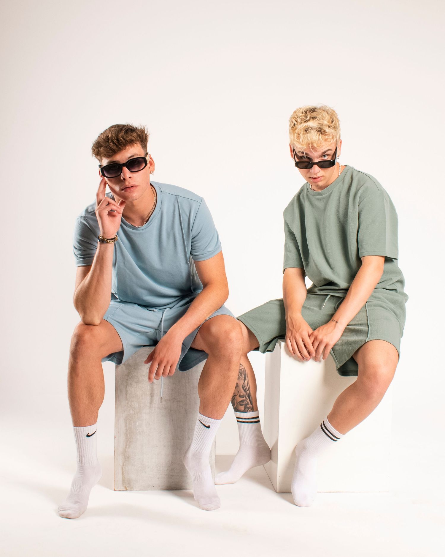 Two young men in casual wear sitting on concrete blocks in a studio setting.