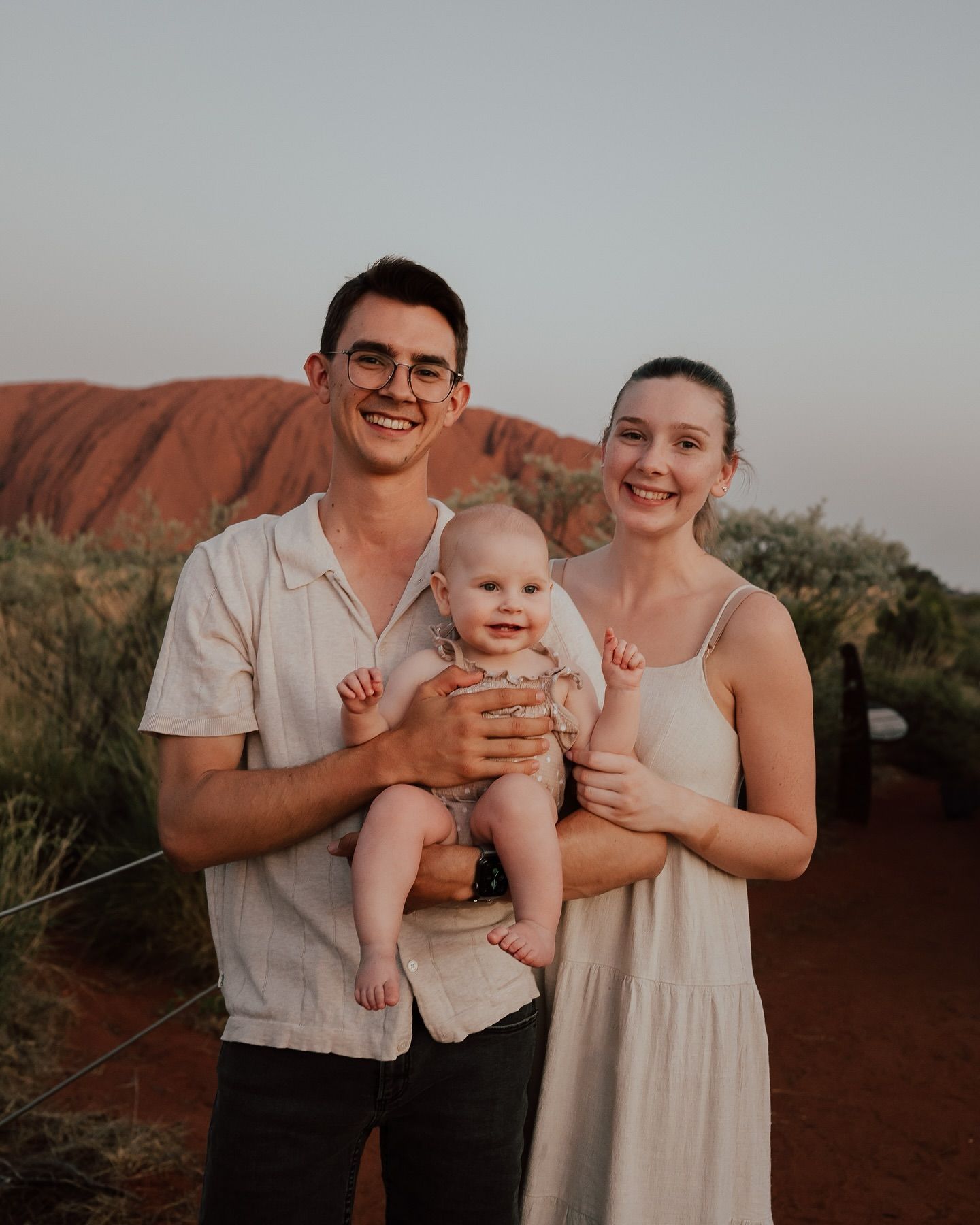 A young couple and their baby standing in front of Uluru