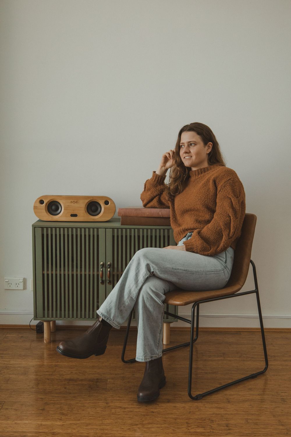 Person in brown sweater lounges in modern chair against white wall with radiator.