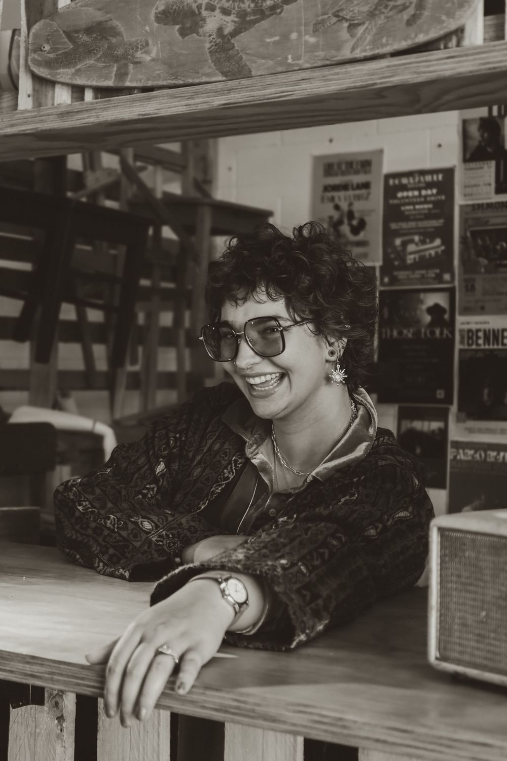 Black and white photo showing someone with curly hair and glasses leaning on a countertop.