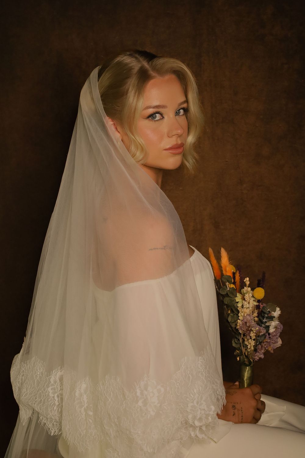 A bride in a white wedding dress and veil poses against a dark background in a series of romantic portraits.