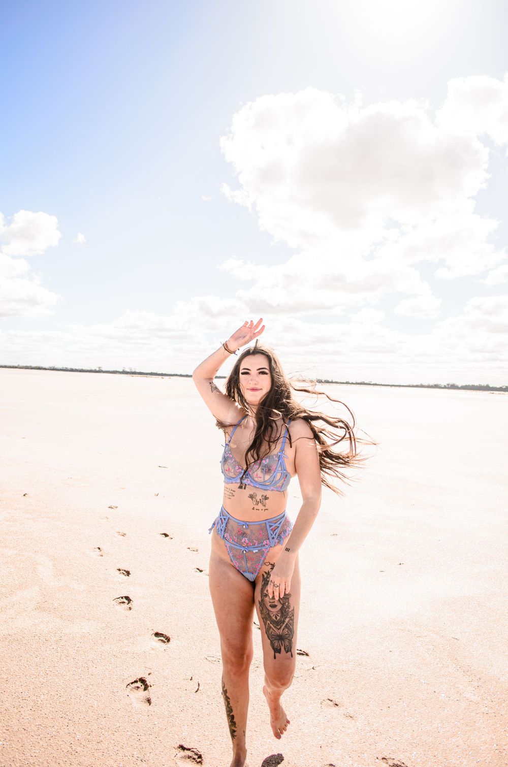 Person in blue swimwear runs playfully on beach with hair flowing in wind.
