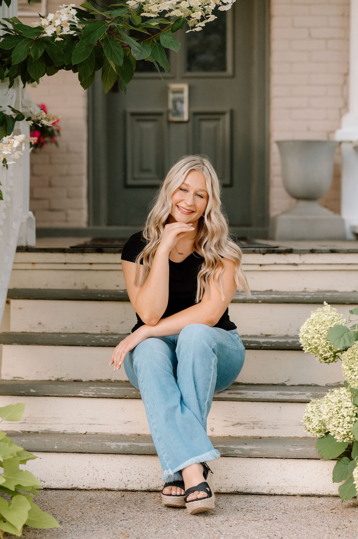A casual portrait of someone relaxing on front porch steps with flowering hydrangea plants.