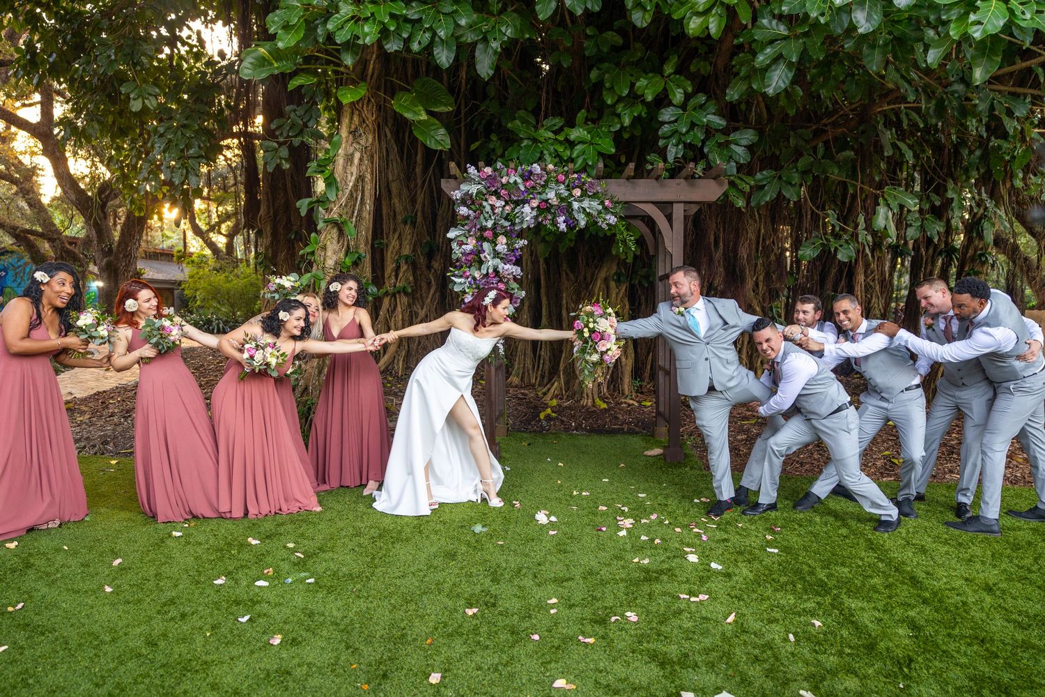 Wedding party poses playfully on grass with bridesmaids and groomsmen.