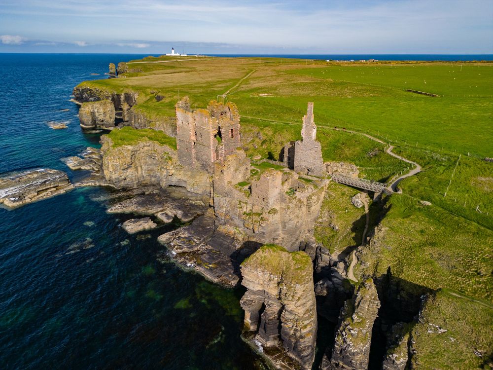 Dramatic aerial views of rugged coastal cliffs with historic lighthouse and buildings perched along the rocky shoreline.