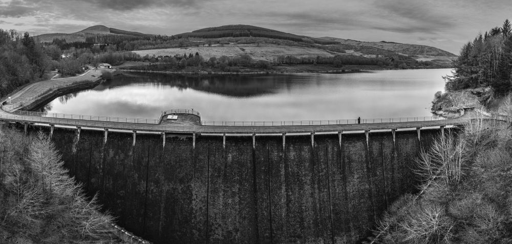 Panoramic black and white landscape view of rolling hills and mountains under dramatic sky.
