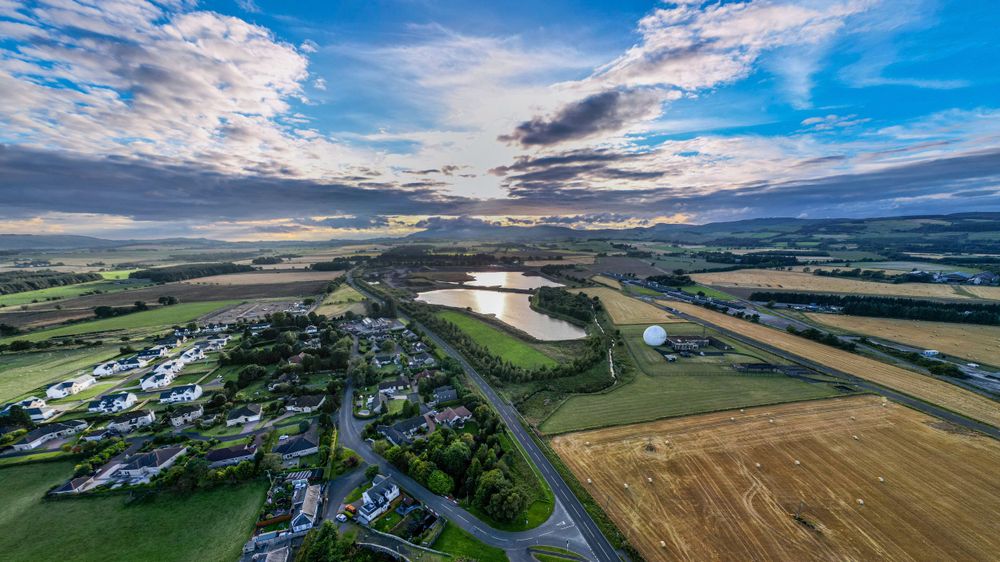 Aerial panorama of rural farmland and countryside under blue sky with scattered clouds.