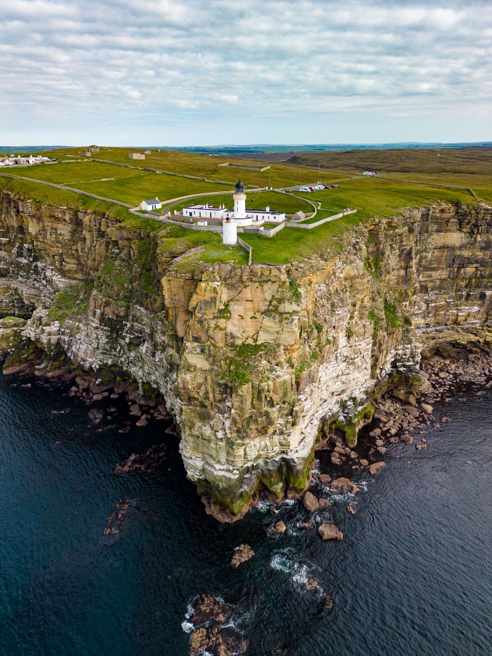Stunning cliffside lighthouse station overlooking the dramatic rocky coastline and crashing waves below.