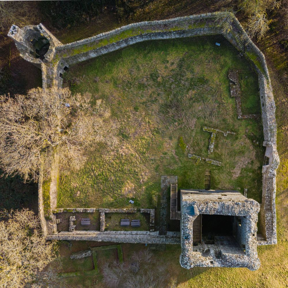 Aerial view of ancient stone ruins and walls surrounded by grass and trees.