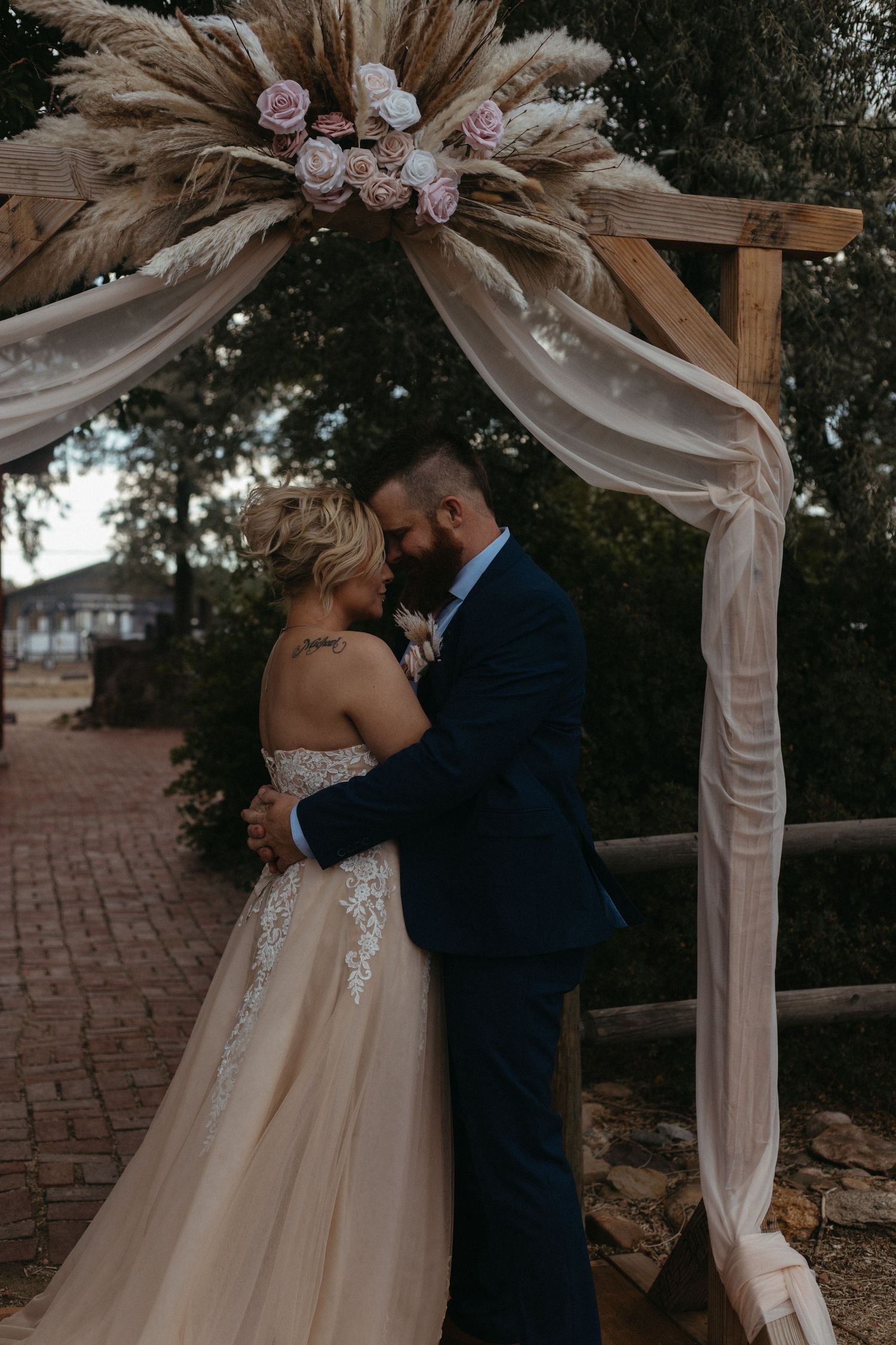 Wedding ceremony under a draped arch decorated with pink flowers and natural greenery.