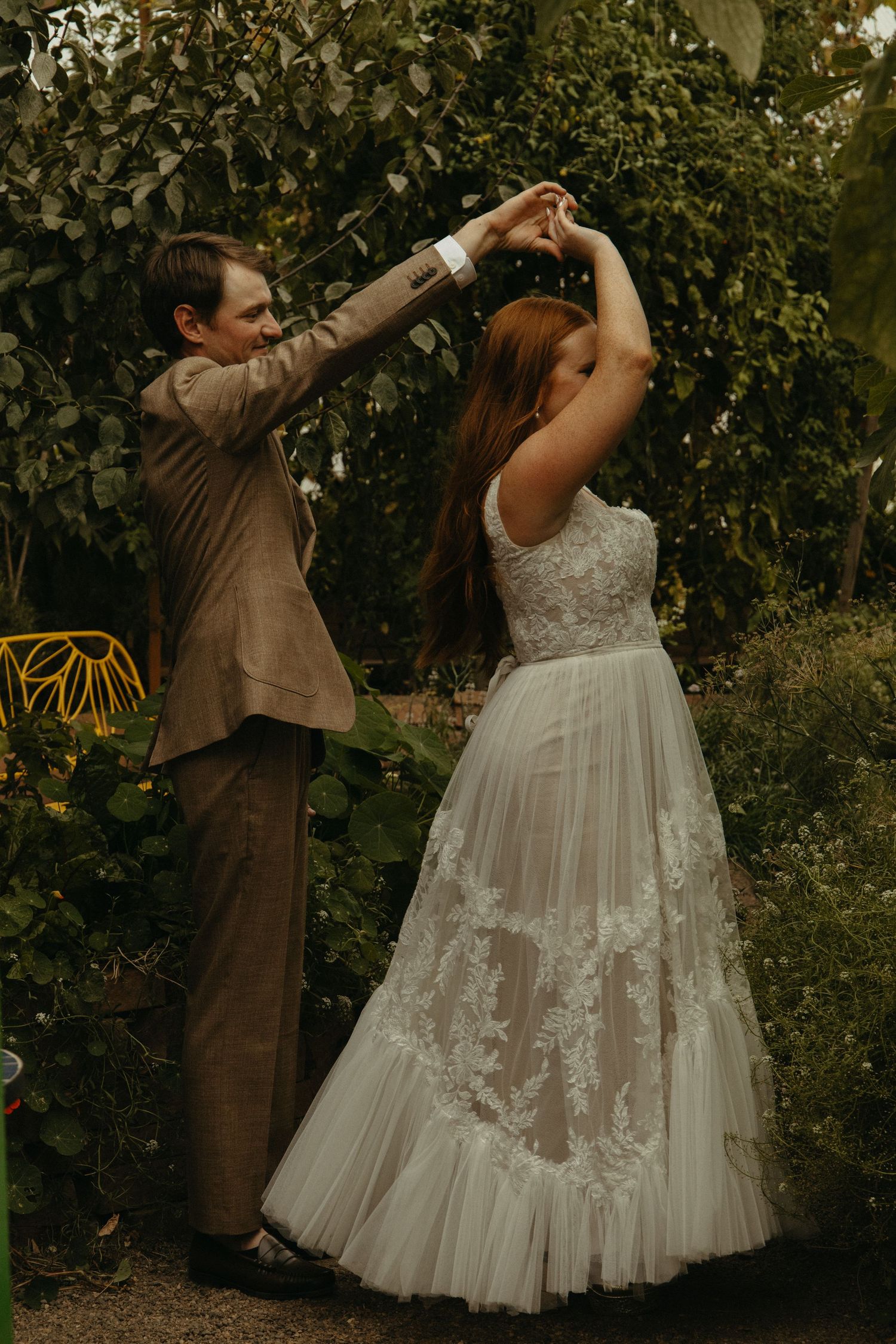 Wedding party performs celebratory dance moves in garden setting with white dress and brown suits.