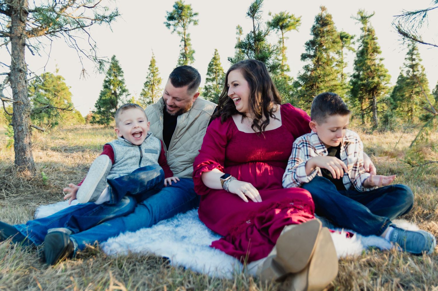 Family of four sitting together on a blanket in a sunny outdoor setting.
