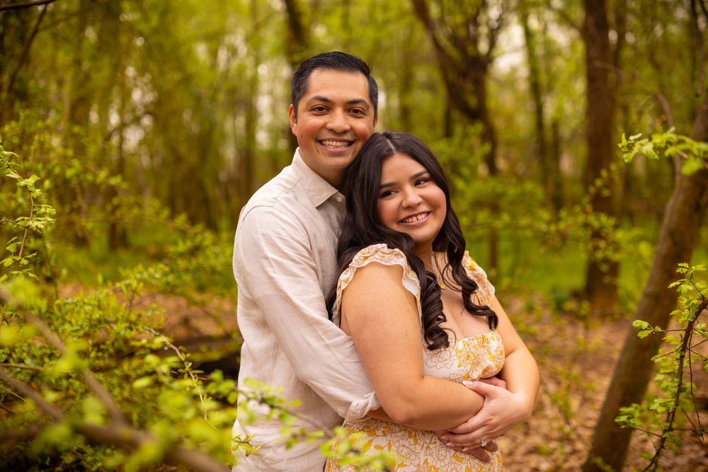 A couple embraces on a wooden log surrounded by green foliage in a forest setting.