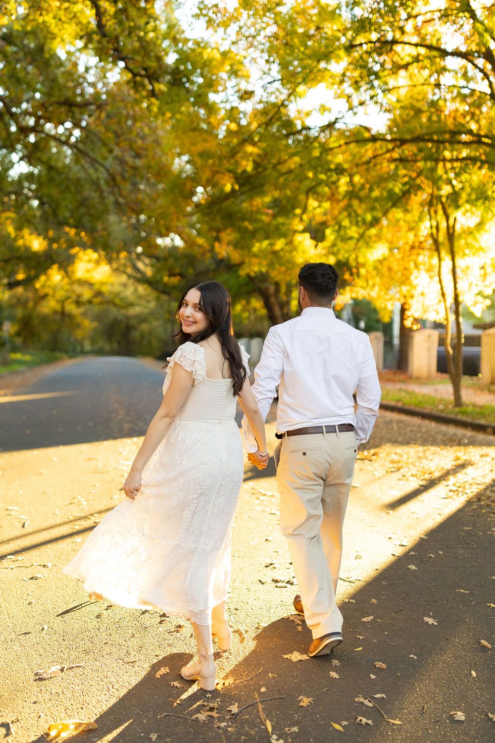 A couple in white outfits walks together during sunset casting long shadows.