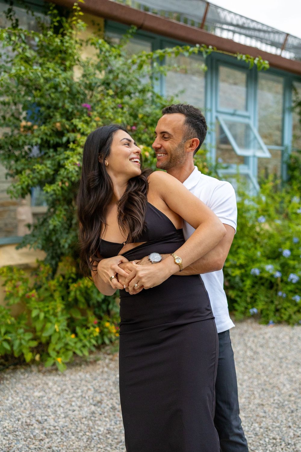 Playful couple laughing and embracing in garden setting wearing black and white outfits.