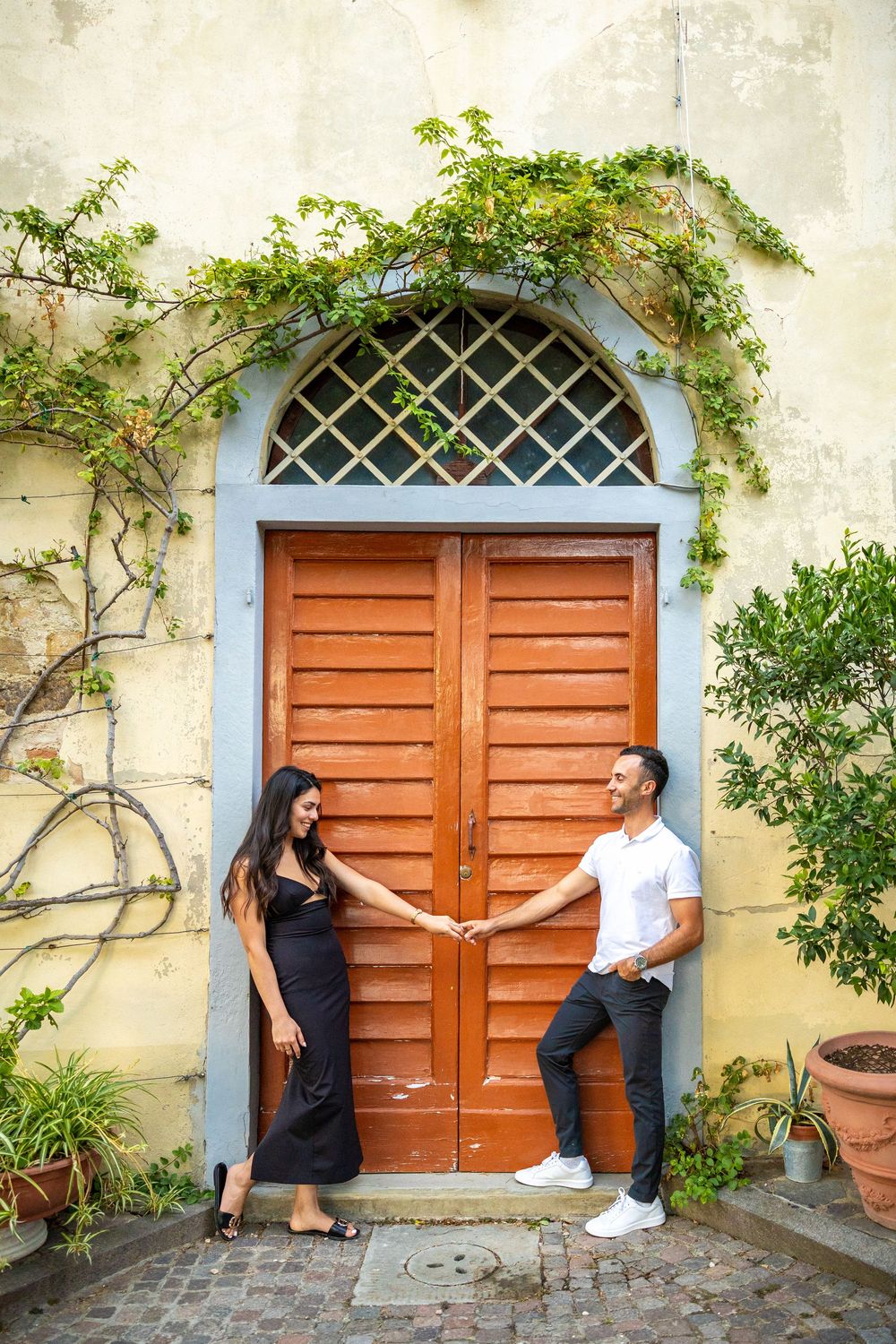 Couple posing playfully by rustic wooden door with climbing vines.