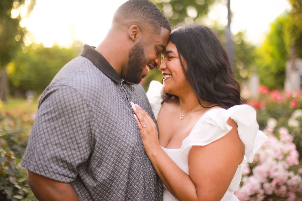 A couple embraces in a sunlit garden with palm trees and flowers in the background.