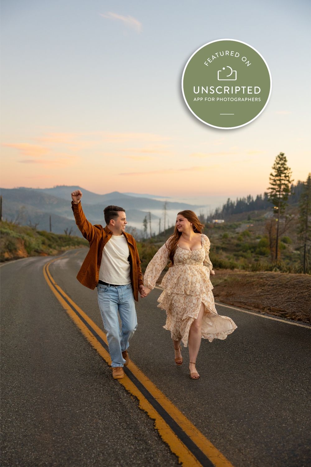 A couple dances and spins joyfully on a mountain road at sunset with evergreen trees and hills in the background.