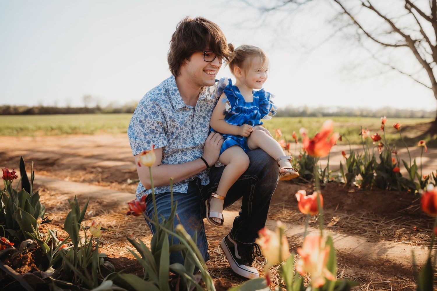 Family enjoying a spring day together outdoors among blooming tulips and flowers in a garden setting.