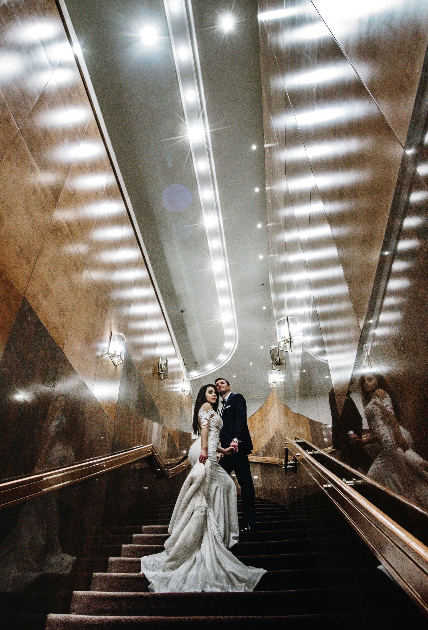 A dramatic wedding photo on illuminated stairs with reflective walls creating a stunning visual effect.