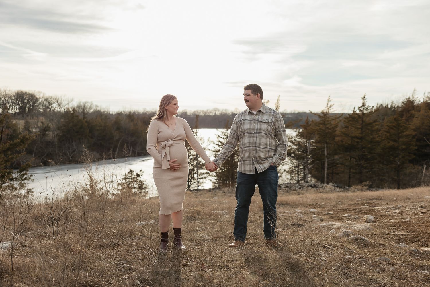 pregnant mother and dad to be holds hands in front of lake olathe during photo session as date night ideas in kansas city