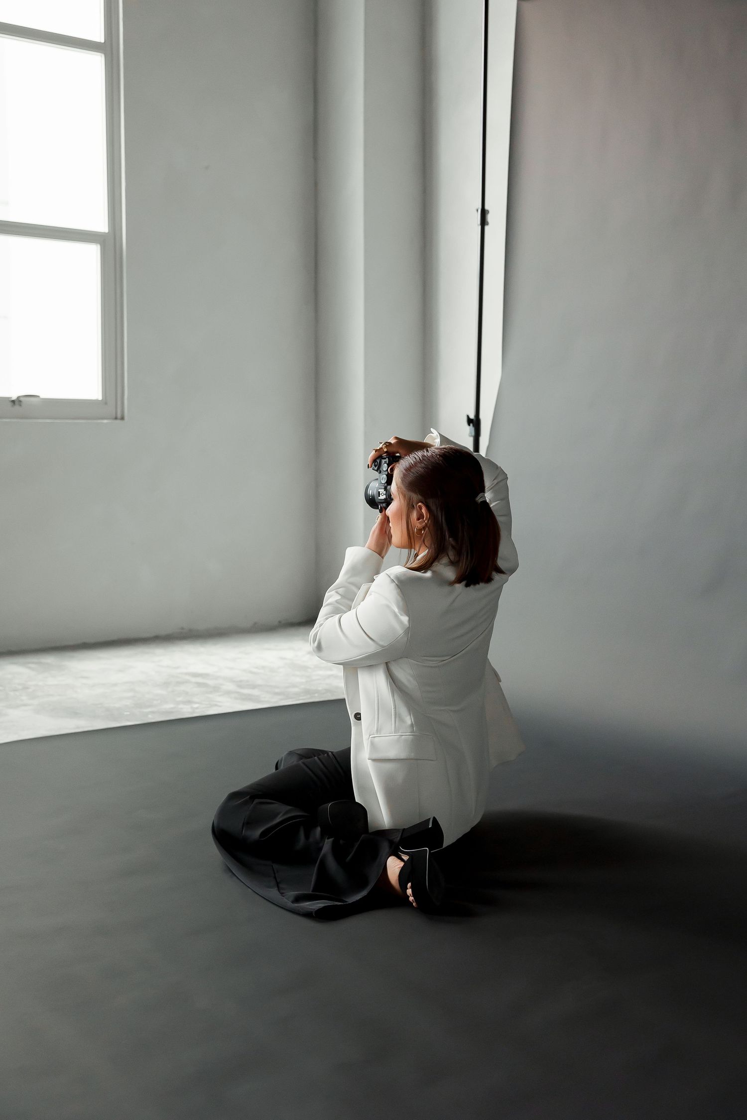 A young girl in a white dress stands in a room, looking out a window.