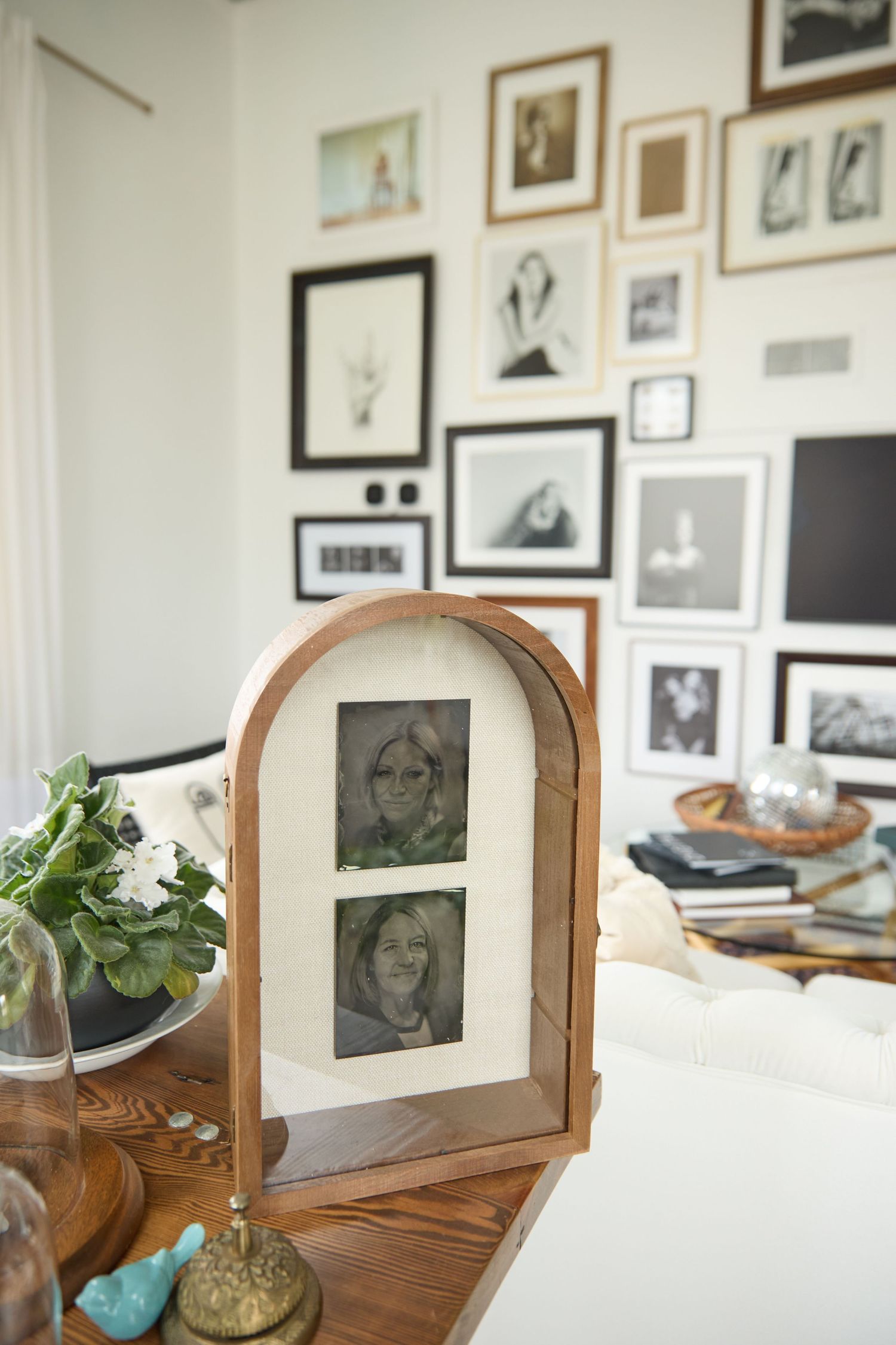 A gallery wall of black and white framed photographs displayed above a wooden dresser with plants and decor.