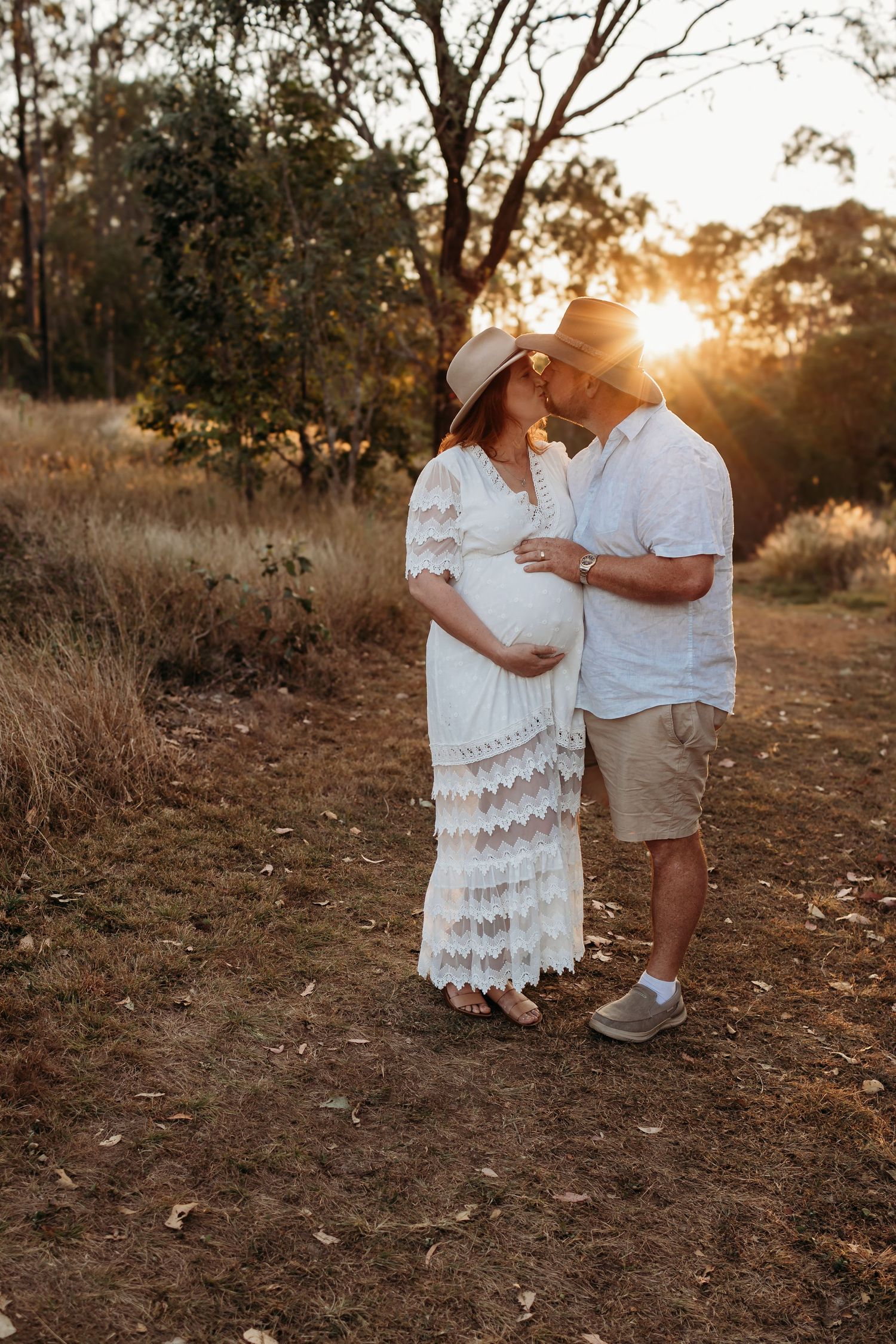 Romantic sunset maternity photo of couple in white dress and casual wear.