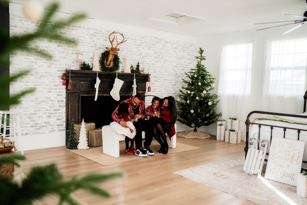 Family in matching red outfits sitting by a decorated fireplace with a Christmas tree in a festive white room.