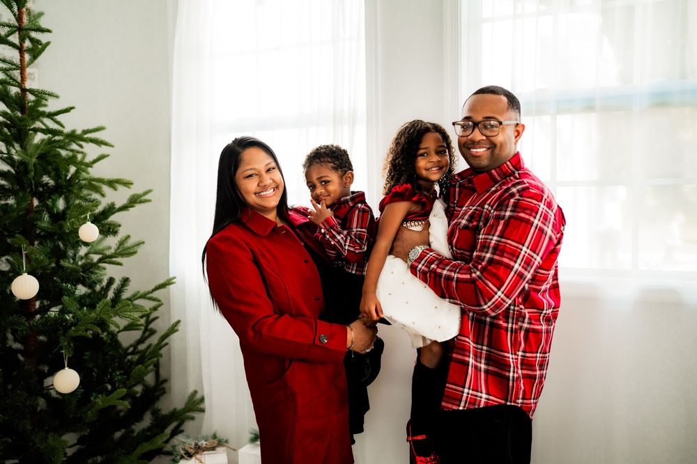Family in matching red outfits smiling by a decorated Christmas tree.