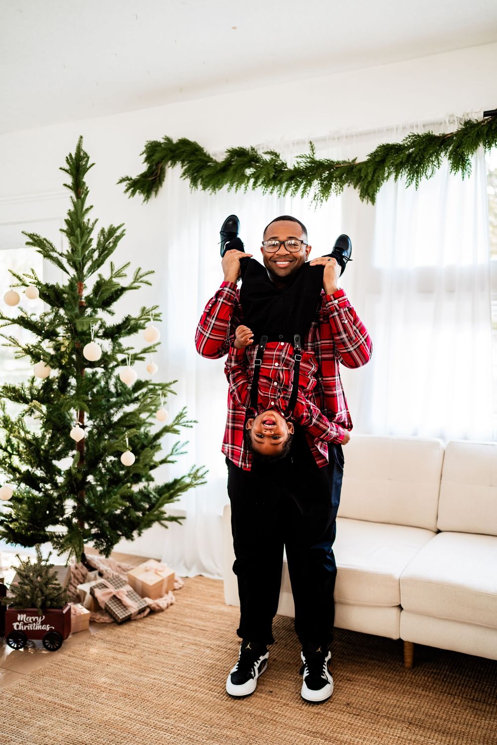 Father playfully holding child upside down near a decorated Christmas tree.