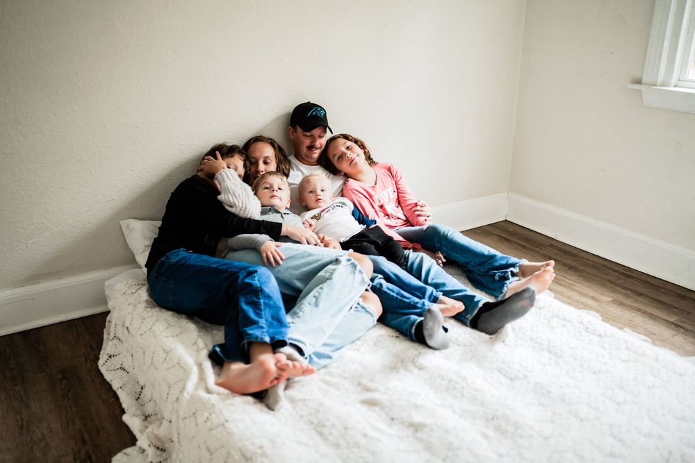 Family of five cuddling together on a white fluffy rug on the floor in a bright minimalist room.