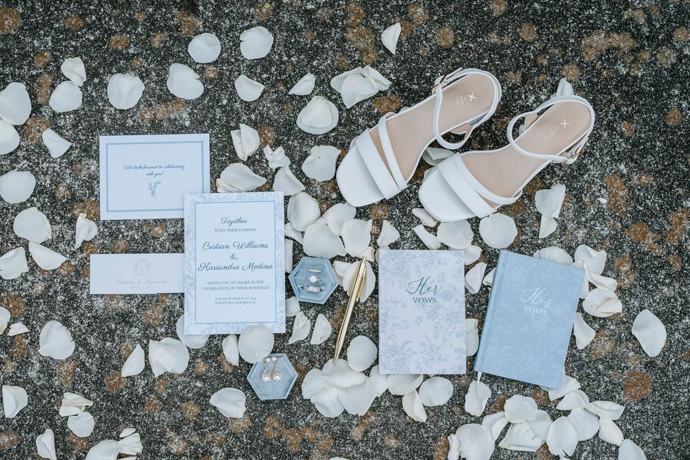 White rose petals and paper confetti scattered across a dark stone surface create a romantic wedding setting.