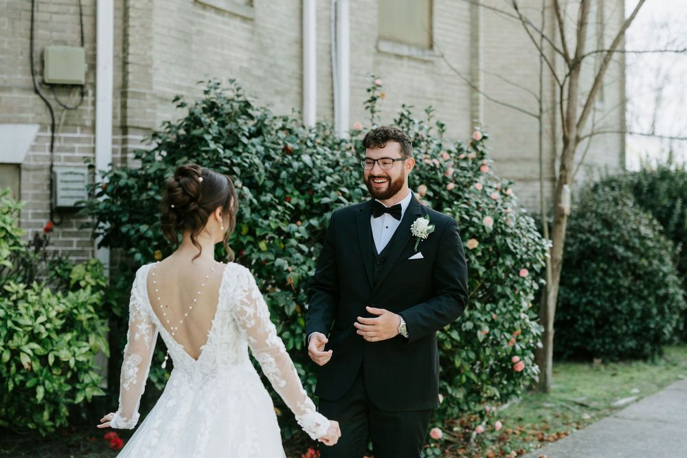 A couple in wedding attire poses together in an outdoor garden setting with lush greenery.