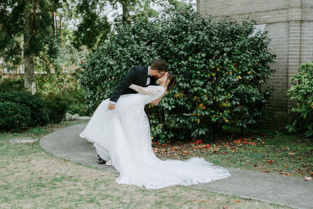 A couple embraces in a garden setting with the bride wearing a flowing white wedding gown with a long train.