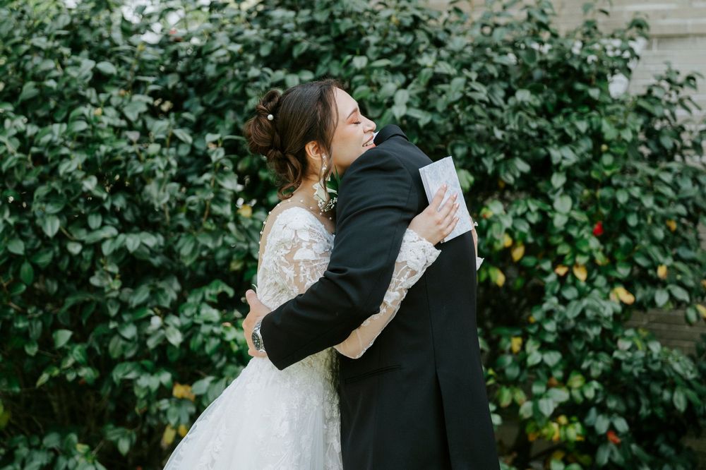 A couple shares an intimate embrace against a backdrop of lush green foliage during their wedding photoshoot.