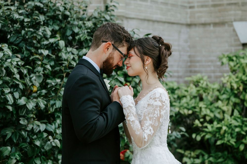 Romantic wedding couple shares intimate moments in a garden setting with brick walls and greenery.