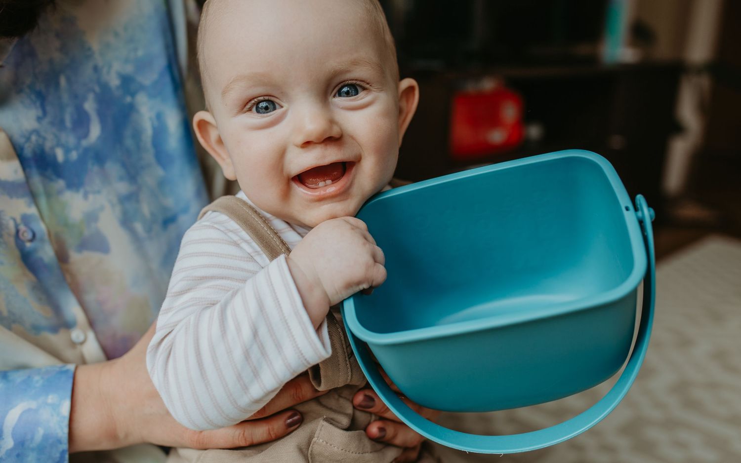 Smiling baby in white striped shirt holding a bright turquoise plastic bucket.